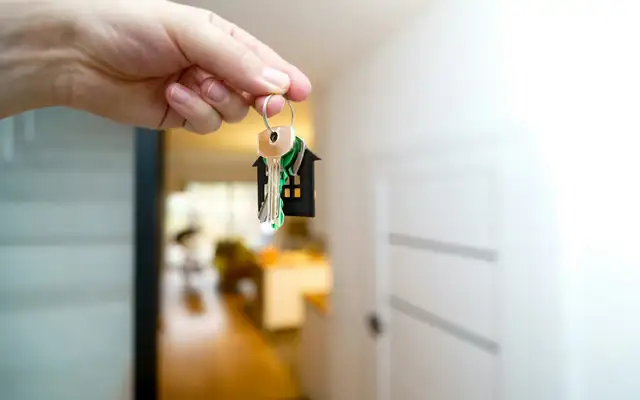 A hand holding a set of house keys at an open front door