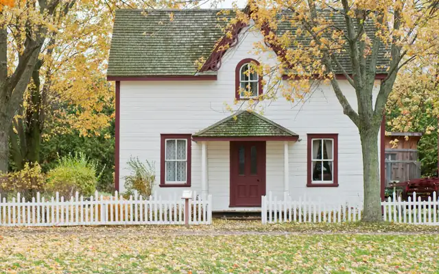 A small white house under maple trees on an autumn day