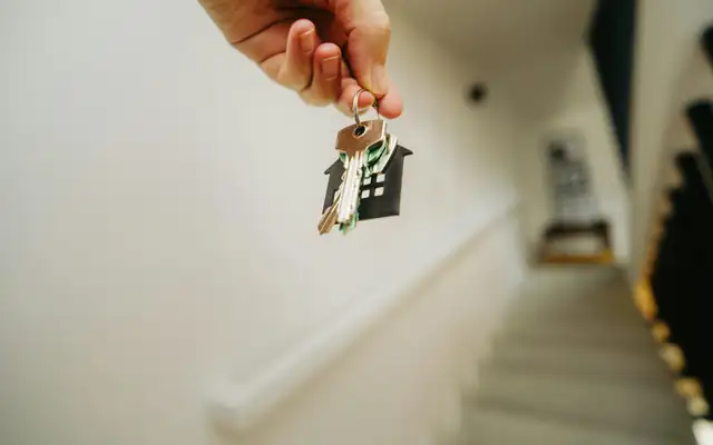 A hand holding a set of house keys on a house-shaped keychain