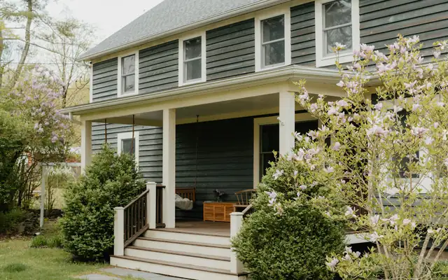 A gray house with a front porch and steps behind a flowering shrub