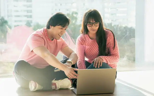 A couple sitting on the floor at home, planning together on a laptop