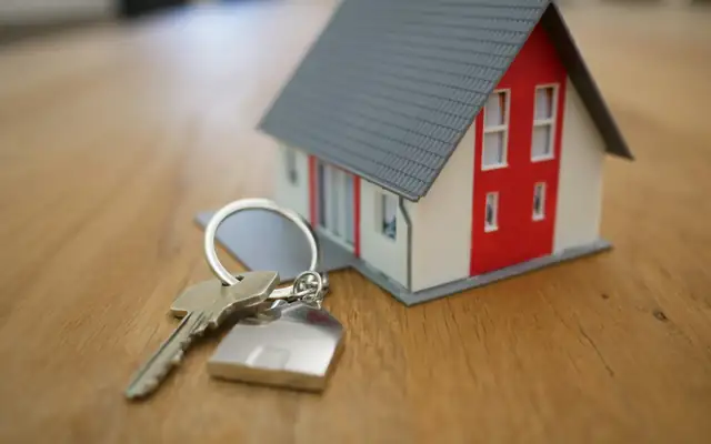 A small model house beside a set of keys on a table
