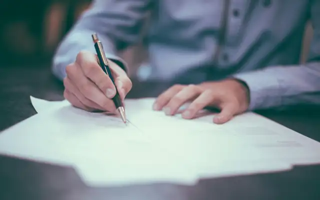 A hand signing a sheet of paper with a pen