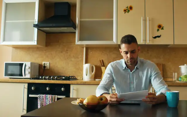 A man reading papers at his kitchen table with a cup of coffee