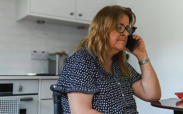 A woman on the phone at her kitchen table
